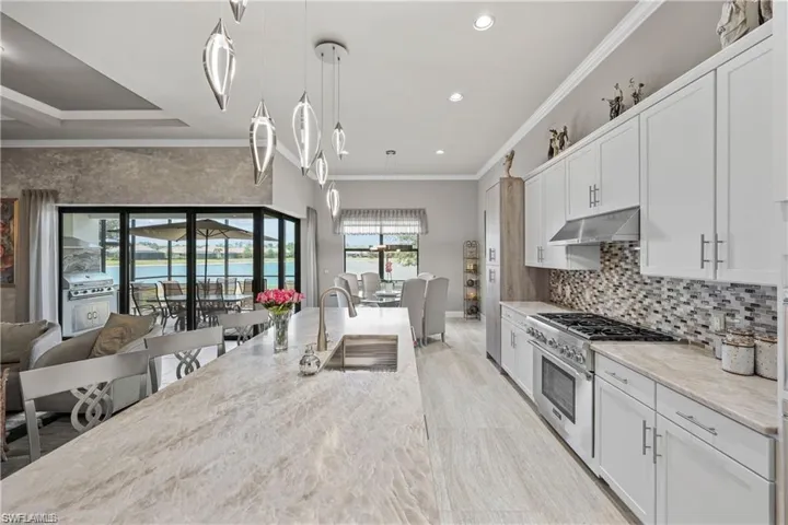 Kitchen featuring stainless steel stove, under cabinet range hood, crown molding, white cabinetry, and pendant lighting