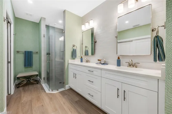 Bathroom featuring double vanity, light wood-type flooring, and a stall shower