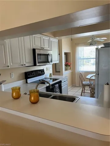 Kitchen featuring white paneled cabinetry, stainless steel microwave, black electric range, and a double-basin stainless steel sink with a high-arc faucet