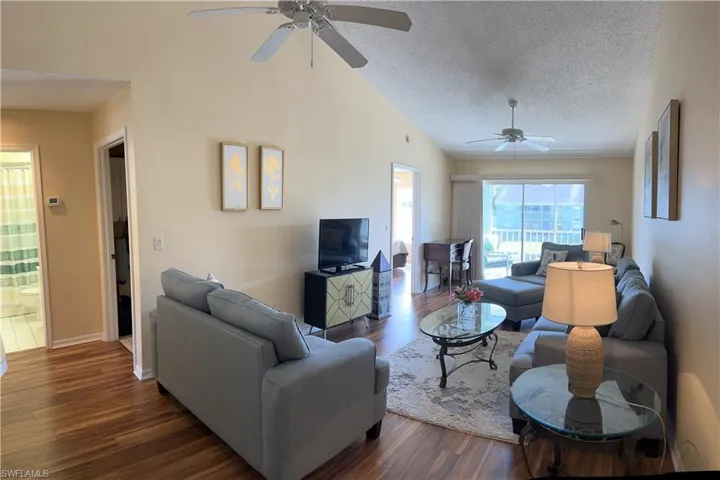 Spacious living area featuring vaulted ceilings, wood-finish flooring, and dual ceiling fans