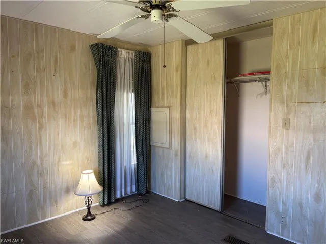 Unfurnished bedroom featuring visible vents, a ceiling fan, dark wood finished floors, a closet, and wooden walls