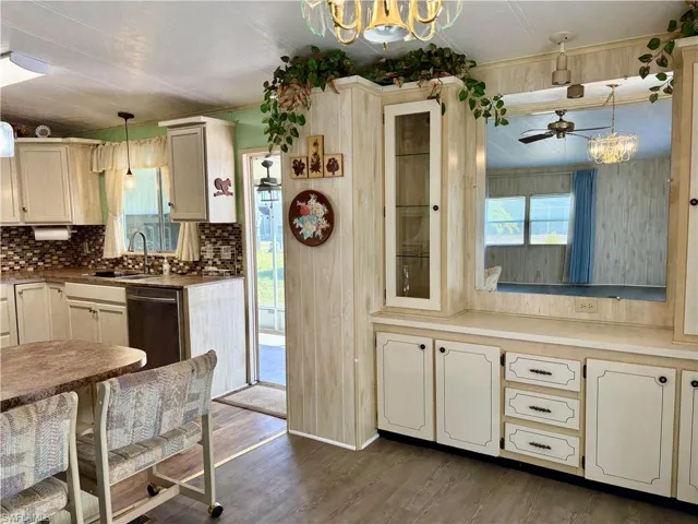 Kitchen with ceiling fan with notable chandelier, a sink, tasteful backsplash, stainless steel dishwasher, and dark wood finished floors