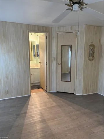 Unfurnished room featuring wooden walls, wood finished floors, baseboards, and ceiling fan