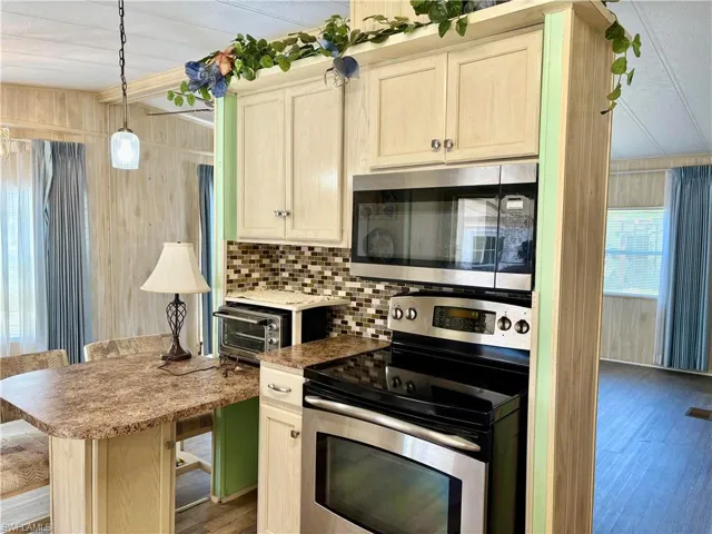 Kitchen featuring backsplash, appliances with stainless steel finishes, a kitchen bar, and wood finished floors