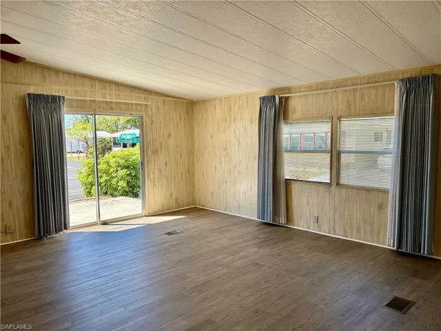 Empty room with wooden walls, visible vents, ceiling fan, lofted ceiling, and wood finished floors