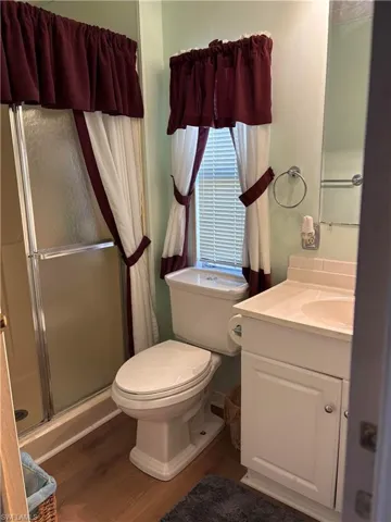 Full bathroom featuring vanity, toilet, wood finished floors, and a stall shower