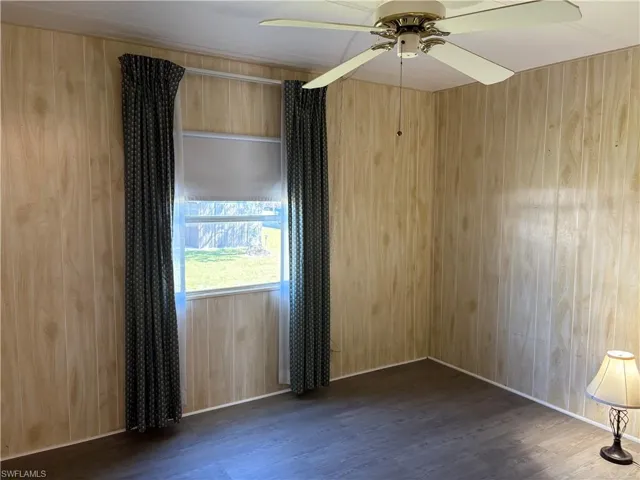 Empty room featuring wood walls, dark wood-type flooring, and a ceiling fan
