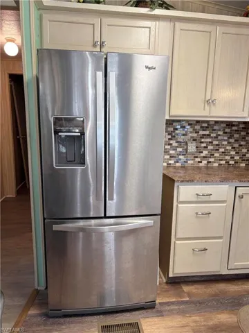 Kitchen featuring decorative backsplash, dark stone counters, dark wood-type flooring, and stainless steel fridge with ice dispenser