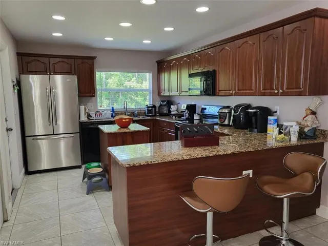 Kitchen with black appliances, sink, light stone counters, kitchen peninsula, and light tile patterned floors