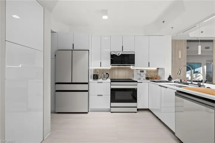 Contemporary kitchen featuring white high-gloss cabinetry, stainless steel appliances, and integrated under-cabinet lighting