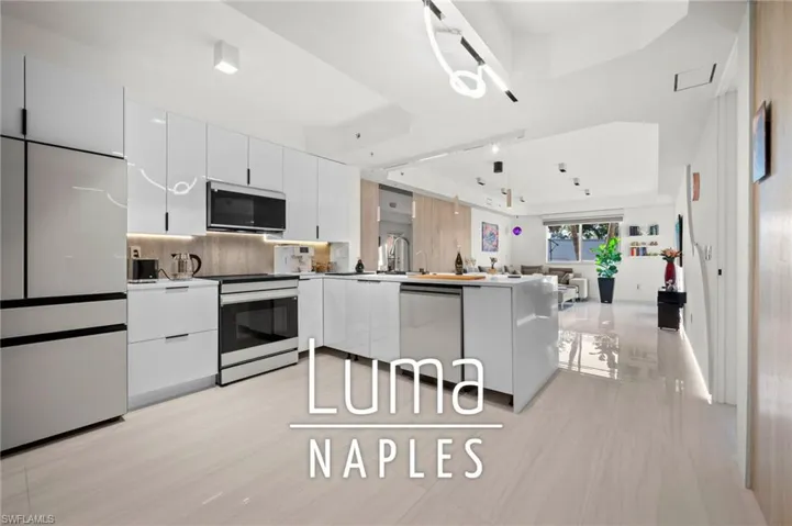 Contemporary kitchen featuring high-gloss white cabinetry, integrated stainless steel appliances, a center island with a built-in dishwasher, and light-toned tile flooring