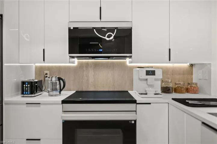 Modern kitchen featuring sleek white cabinetry with black hardware, a built-in oven, and a flat cooktop