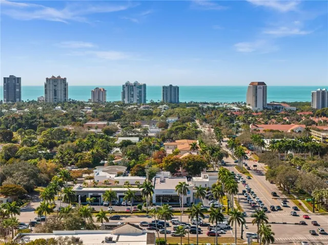 Aerial perspective showcasing the vibrant coastal area with prominent high-rise buildings, lush green landscaping, and the expansive turquoise ocean