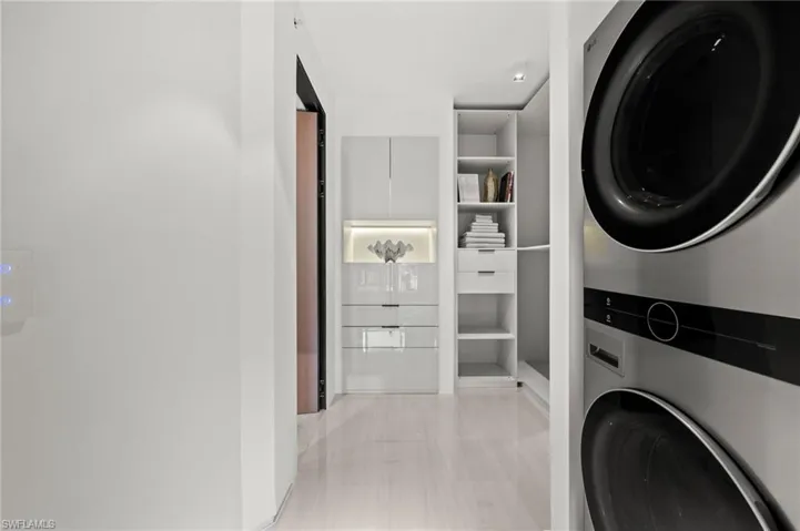 Integrated laundry center featuring a stacked washer and dryer, light wood-finish flooring, built-in shelving, recessed lighting, and a contemporary light switch panel