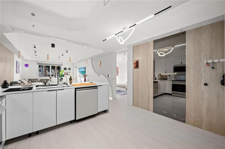 Modern kitchen featuring white flat-panel cabinetry, a stainless steel dishwasher, and a black sink with a wall-mounted faucet