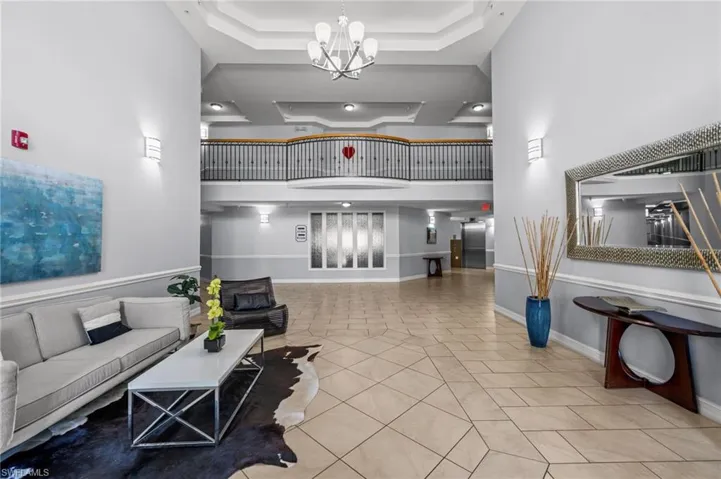 Two-story foyer featuring a contemporary chandelier, geometric tile flooring, tray ceilings, and a second-level balcony with metal balusters