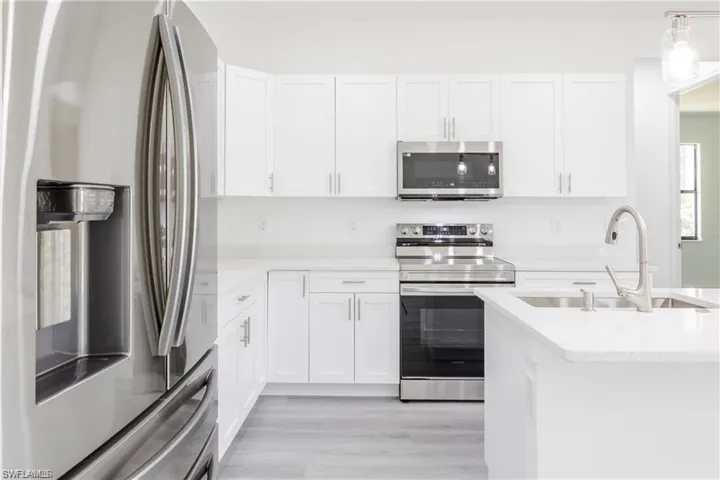 Kitchen featuring stainless steel appliances, white cabinets, light stone counters, hanging light fixtures, and light wood-style floors