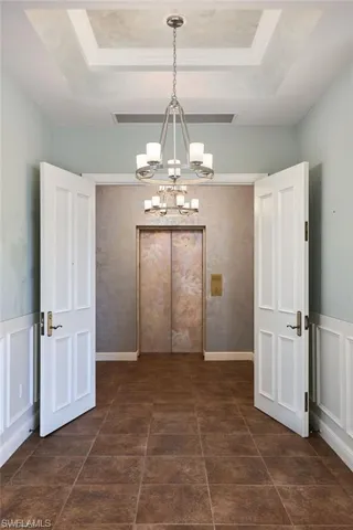 Unfurnished dining area with a tray ceiling, dark tile patterned floors, and an inviting chandelier
