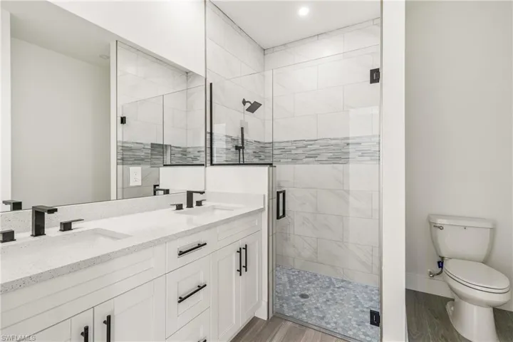 Full bath featuring a shower stall, double vanity, and light wood-type flooring