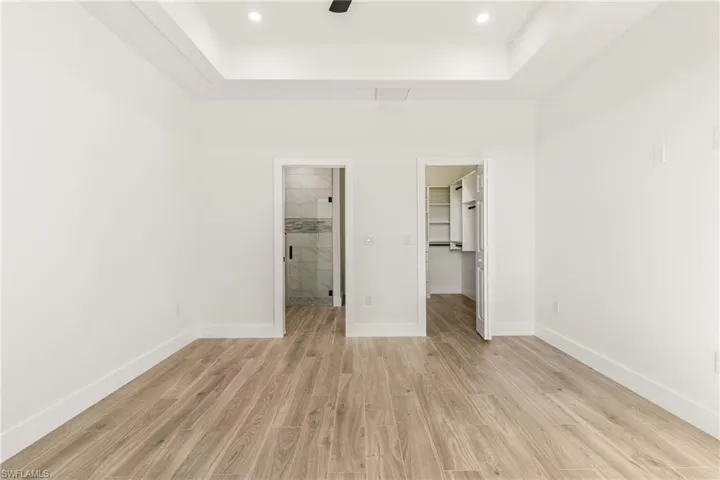 Unfurnished bedroom featuring a walk in closet, a raised ceiling, light wood-style floors, connected bathroom, and recessed lighting