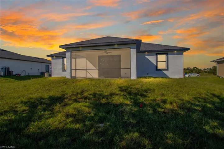 Back of property at dusk with a lawn, stucco siding, and ceiling fan
