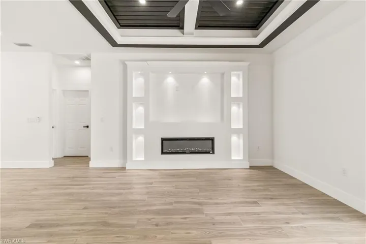 Unfurnished living room featuring ceiling fan, a glass covered fireplace, light wood-type flooring, recessed lighting, and beamed ceiling