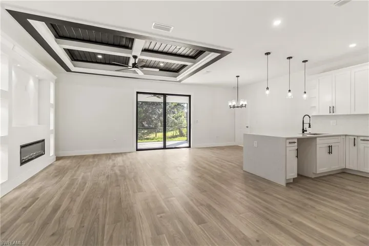 Kitchen featuring a chandelier, pendant lighting, beam ceiling, white cabinetry, and a fireplace