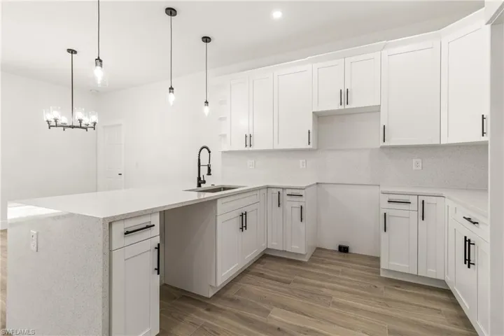 Kitchen featuring a peninsula, light wood-style flooring, white cabinetry, decorative backsplash, and light stone counters