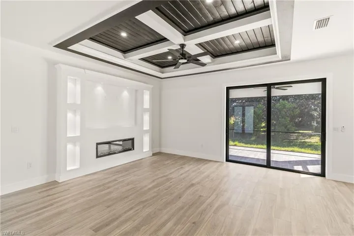 Unfurnished living room with a glass covered fireplace, light wood-type flooring, ceiling fan, coffered ceiling, and recessed lighting