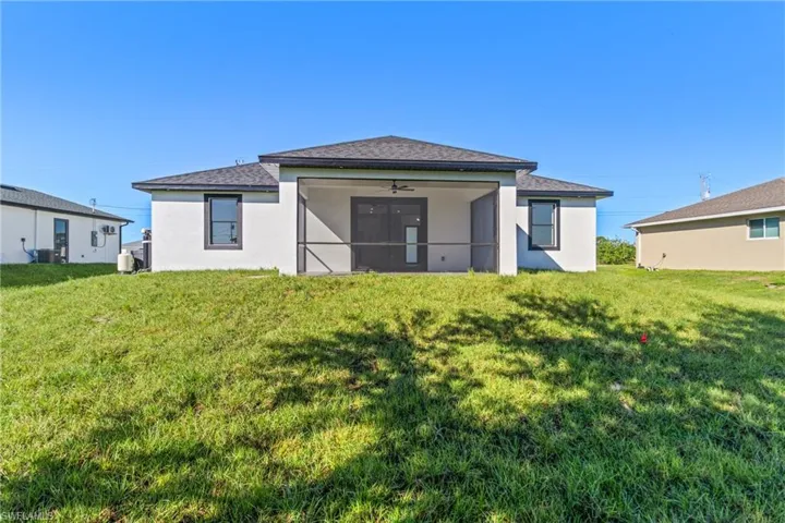 Rear view of property featuring a lawn, a ceiling fan, stucco siding, and a sunroom