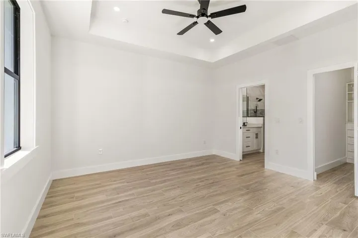 Unfurnished bedroom with a raised ceiling, light wood-style floors, a ceiling fan, a spacious closet, and recessed lighting