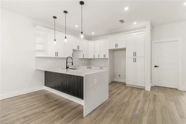Kitchen featuring open shelves, a peninsula, white cabinetry, light stone counters, and a kitchen bar