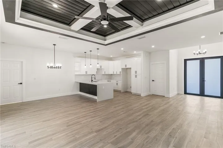 Unfurnished living room featuring a chandelier, coffered ceiling, recessed lighting, light wood-type flooring, and beam ceiling