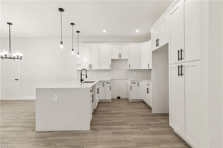 Kitchen featuring white cabinets, decorative light fixtures, light wood finished floors, light stone countertops, and tasteful backsplash