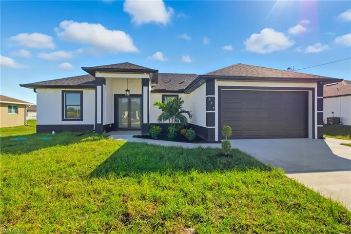 View of front facade featuring a front yard, concrete driveway, stucco siding, a garage, and roof with shingles