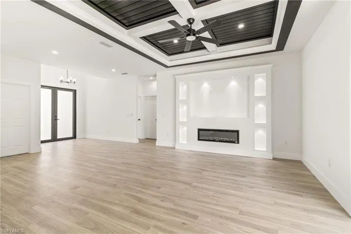Unfurnished living room with ceiling fan, light wood-style flooring, coffered ceiling, a glass covered fireplace, and beamed ceiling