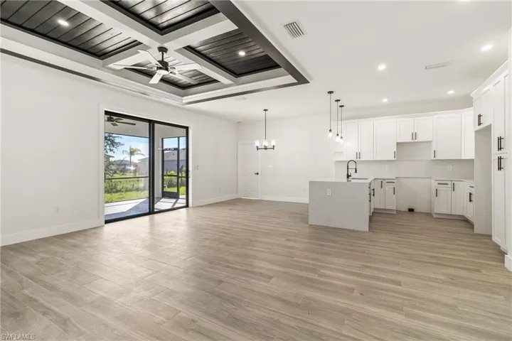 Unfurnished living room featuring a chandelier, light wood-style flooring, beam ceiling, recessed lighting, and coffered ceiling