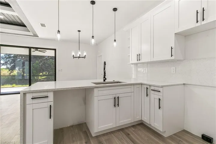 Kitchen with light stone countertops, a peninsula, light wood-style flooring, white cabinetry, and open shelves