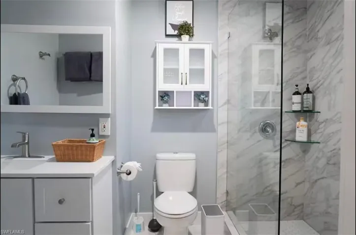Bathroom featuring a glass-enclosed shower with marble-look wall tiling and integrated glass shelving