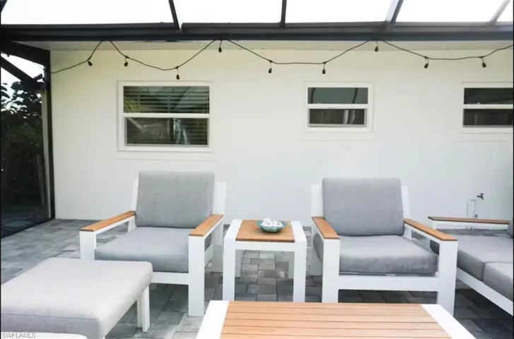 Outdoor living area featuring a covered patio, white stucco exterior, multiple windows with blinds, and string lighting