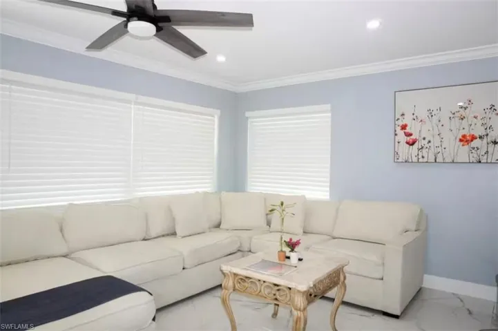 Spacious living area featuring light blue walls, white crown molding, and large windows with white horizontal blinds