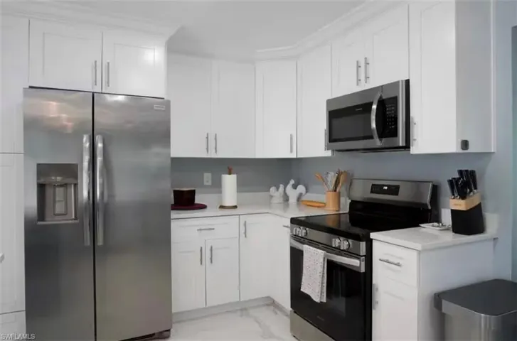 Modern kitchen featuring white shaker cabinetry, stainless steel appliances, light countertops, and light tile flooring