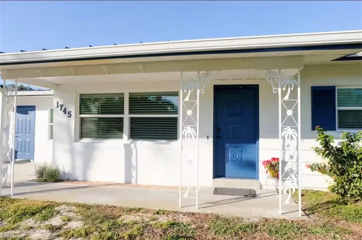 White exterior featuring a covered entry, decorative metal support columns with palm tree motifs, a blue front door, and blue window shutters