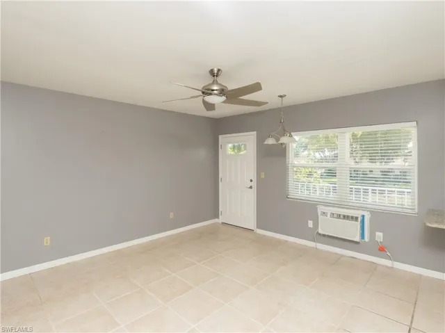 Spacious room featuring tile flooring, neutral wall tones, a ceiling fan with integrated lighting, a white entrance door with decorative glass, and a large window with horizontal blinds