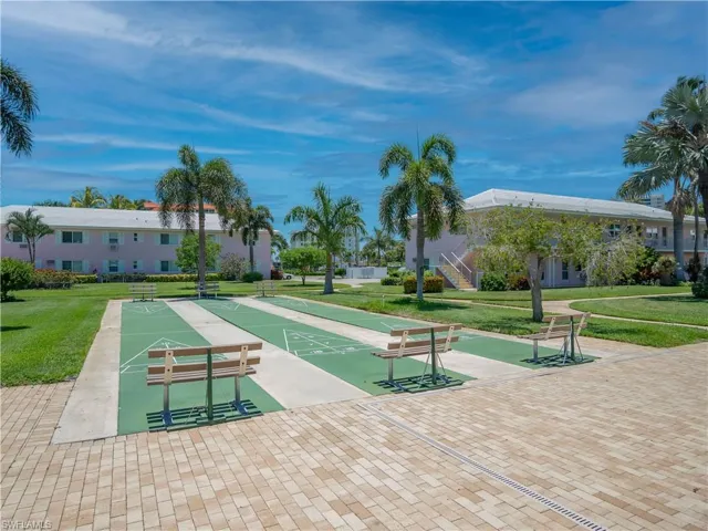 Multiple outdoor shuffleboard courts with accompanying benches, surrounded by mature palm trees and manicured lawns