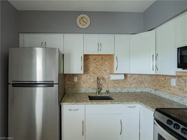Kitchen featuring white cabinetry with brushed nickel hardware, light granite countertops, and a full tile backsplash