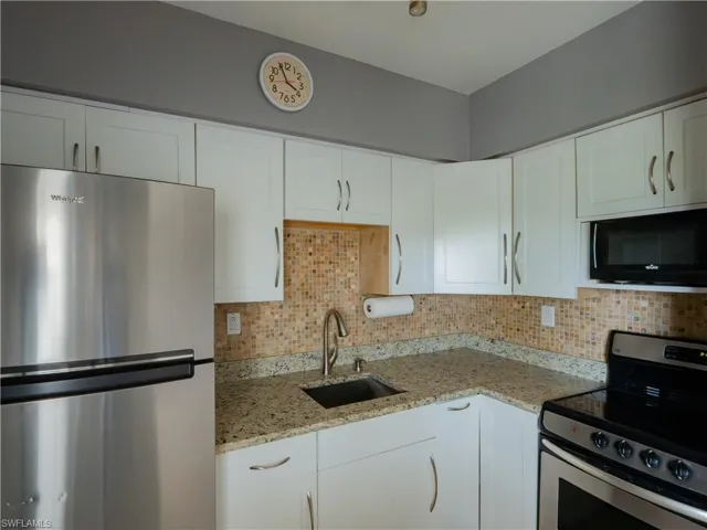Corner kitchen with white cabinetry, stainless steel appliances, speckled countertops, and a mosaic tile backsplash