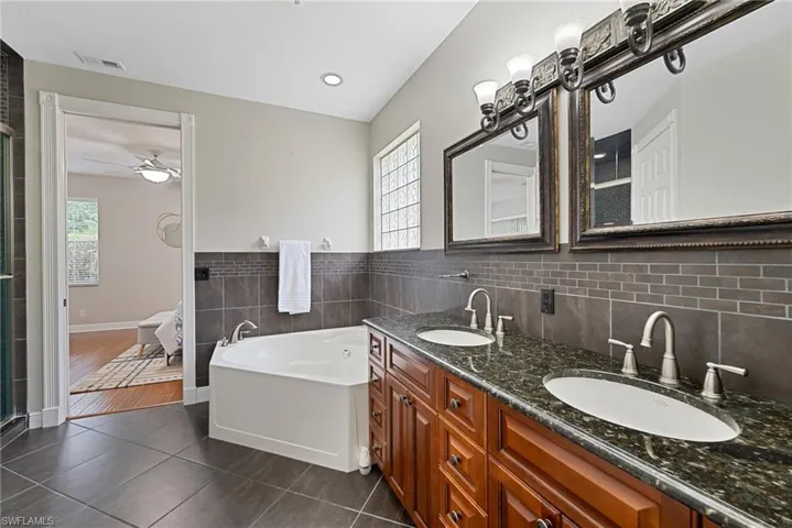 Bathroom featuring tile walls, double vanity, a garden tub, dark tile patterned floors, and a wainscoted wall