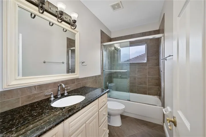 Full bath with combined bath / shower with glass door, vanity, dark tile patterned flooring, and tile walls