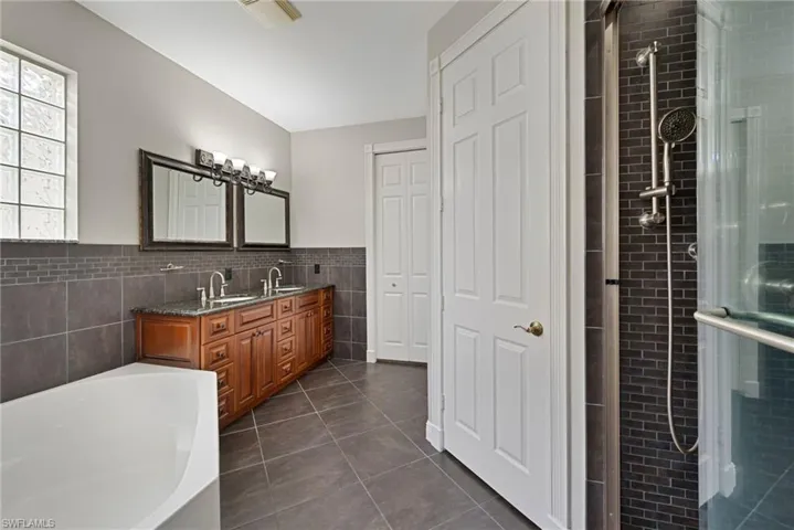 Bathroom with tile walls, a shower stall, a garden tub, double vanity, and a wainscoted wall